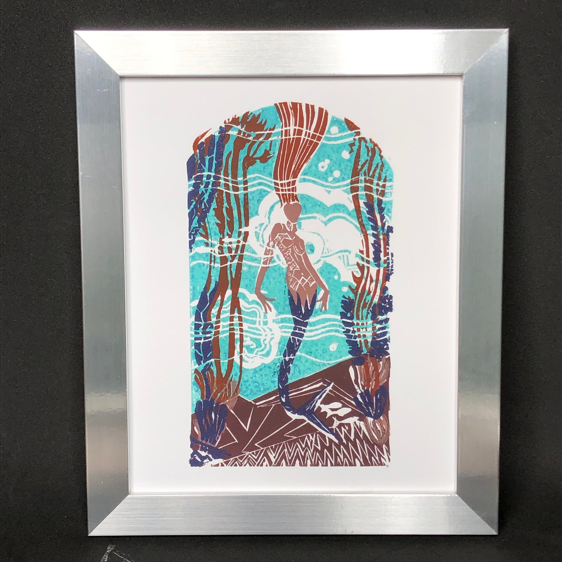 Casino mermaid giclée print of original 5-plate linocut depicting an art deco tile mosaic of the Catalina Casino Mermaid. Bright turquoise back ground with white water movement, stylized mermaid's purple tail surrounded by stylized kelp, coral, and fish. Print is in a silver frame.