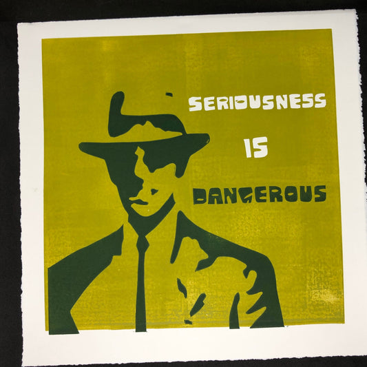 White and forest green text reads: 'Seriousness is Dangerous' to the right of a midcentury modern man dressed up in a suit and tie, donning a fedora hat.  The man is forest green on olive green background.